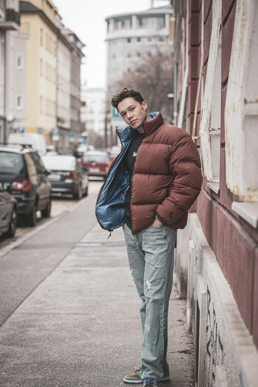 man in red jacket and gray pants standing on sidewalk during daytime