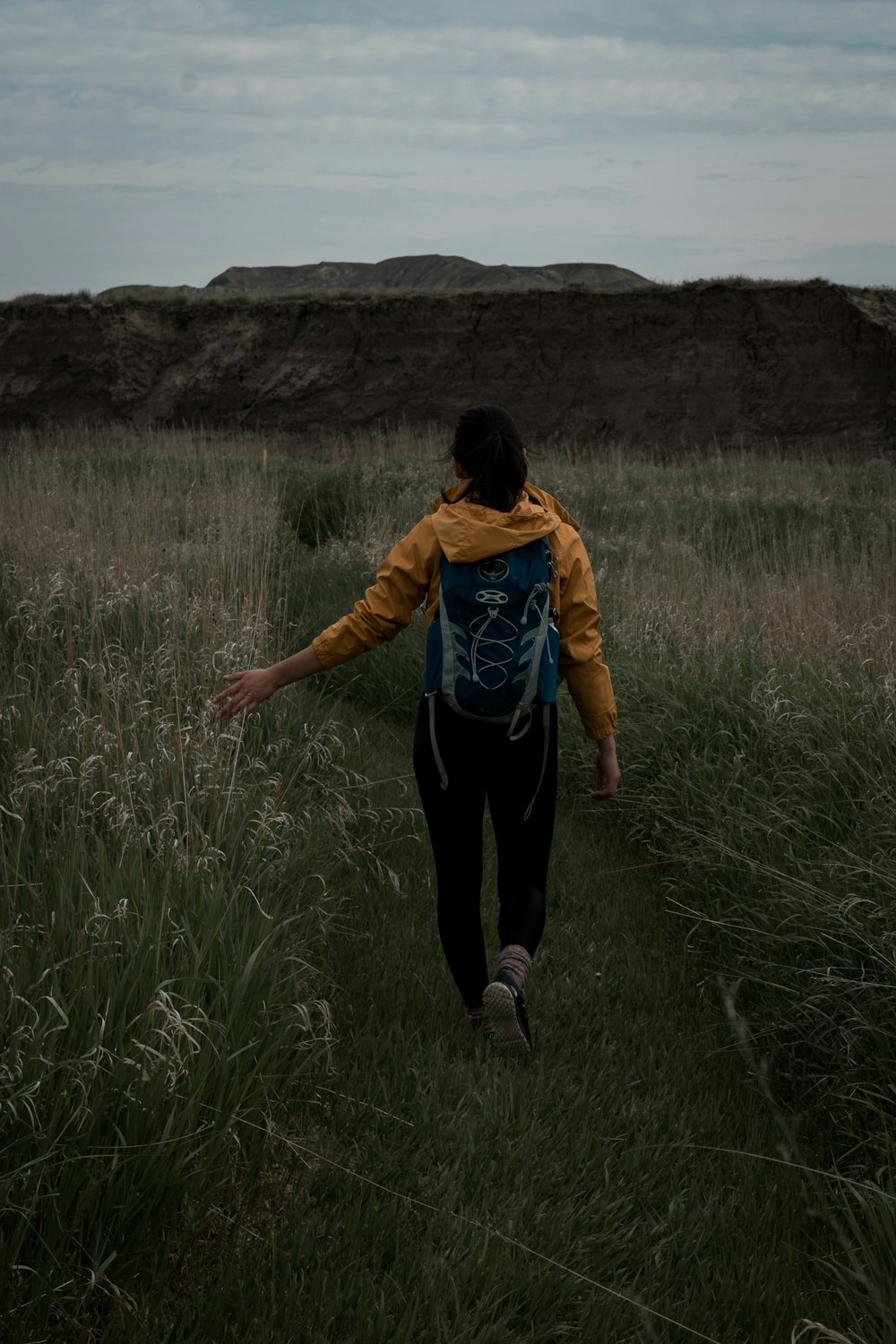 woman in yellow jacket and black pants walking on green grass field during daytime