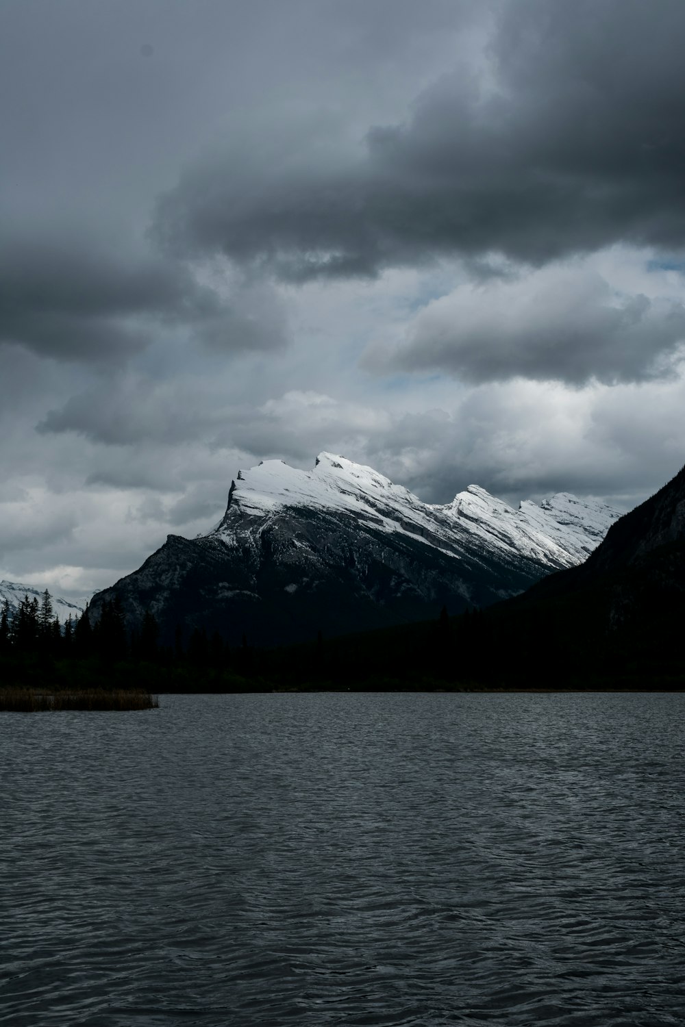 snow covered mountain near body of water under cloudy sky during daytime