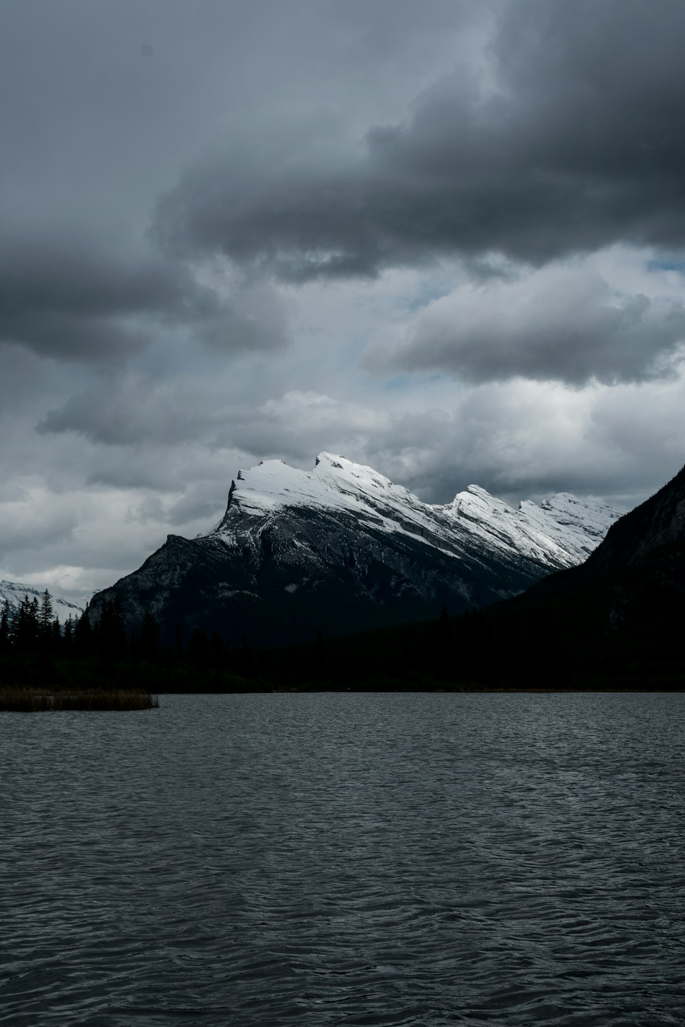 montagne enneigée près d’un plan d’eau sous un ciel nuageux pendant la journée