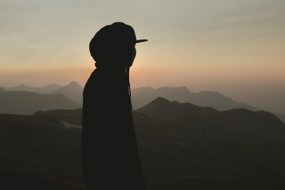 silhouette of woman standing on mountain during sunset