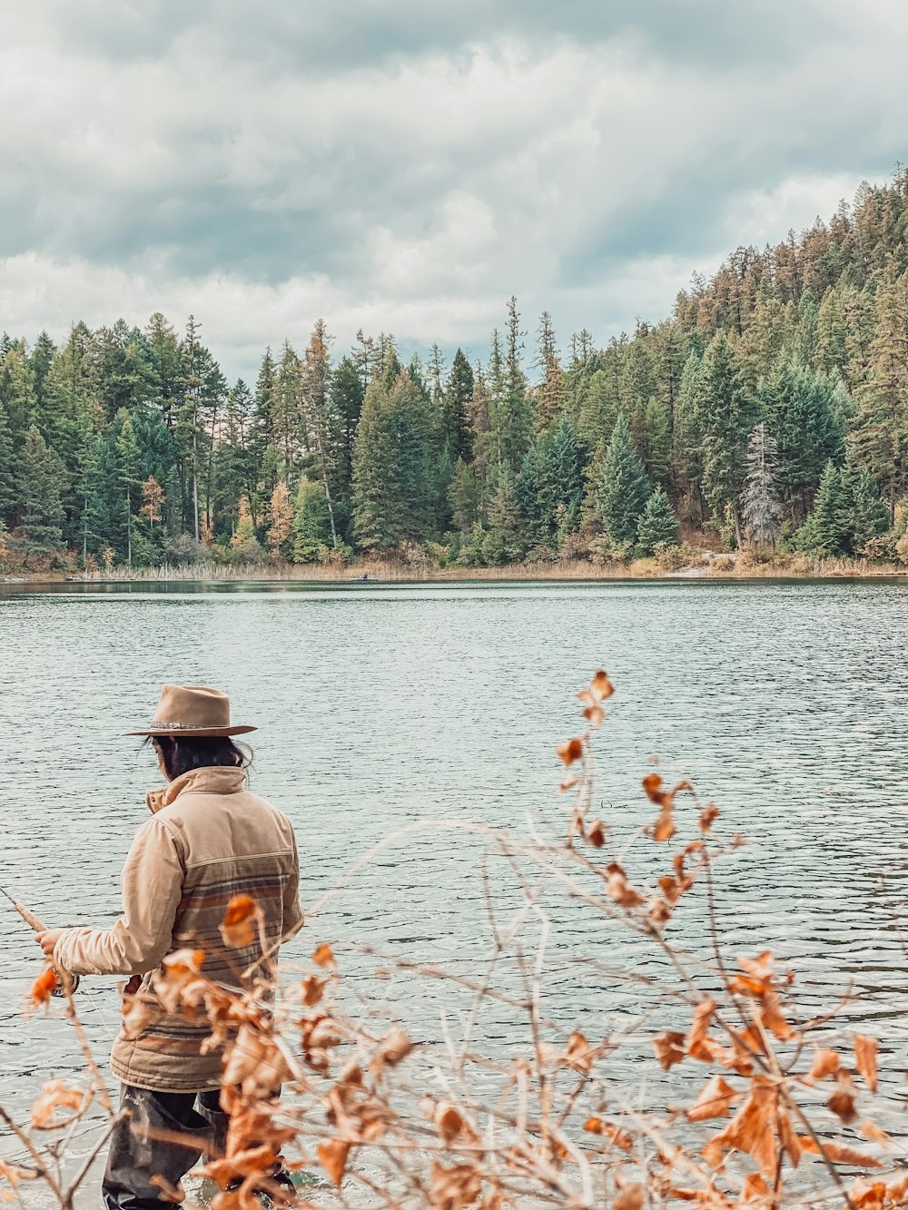 昼間の湖で釣りをする茶色のジャケットを着た男