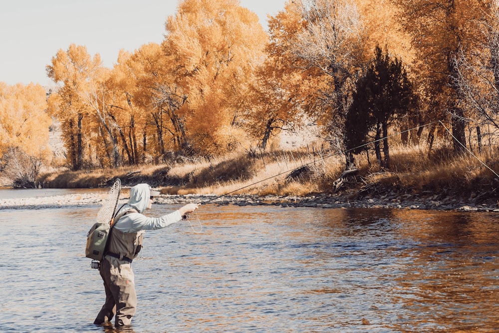 man in white jacket and black pants standing on brown tree branch near body of water