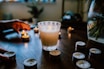 A cozy scene with several lit candles of different shapes and sizes on a wooden table surrounded by raw candle-making materials.
