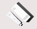 A white rectangular box and a corresponding white tube labeled 'Act + Acre Restorative Hair Mask' are arranged on a light beige background. The box has a minimalist design with black text. The tube and its cap are placed in a diagonal position relative to the box.