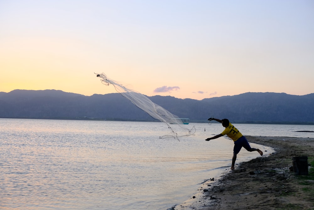 man in yellow shirt and black pants holding fishing rod on beach during daytime