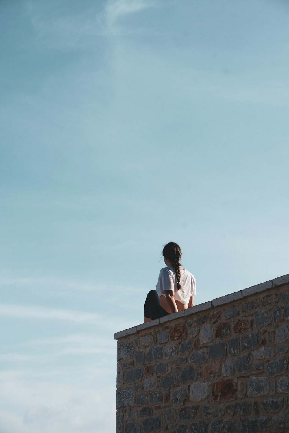 man in white t-shirt sitting on brown concrete wall during daytime