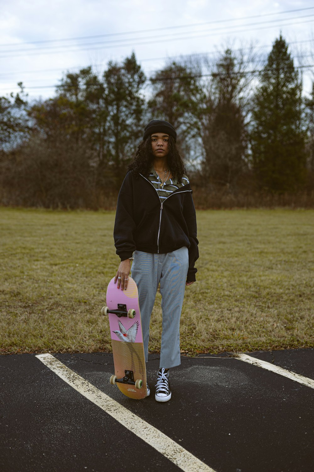 woman in black jacket and blue denim jeans holding pink and white skateboard