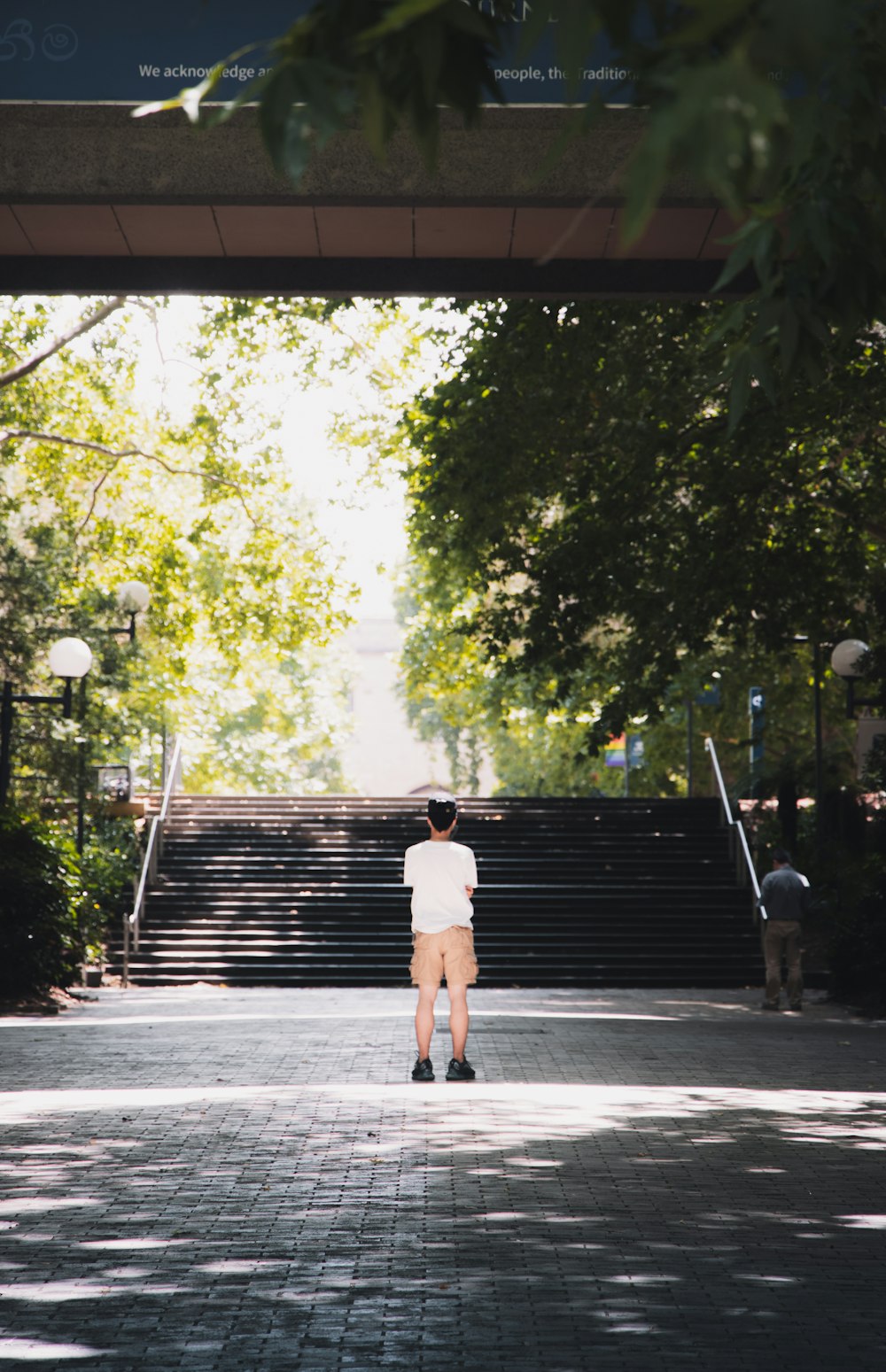 흰색 티셔츠와 갈색 반바지를 입은 남자가 낮 동안 보도를 걷고 있다