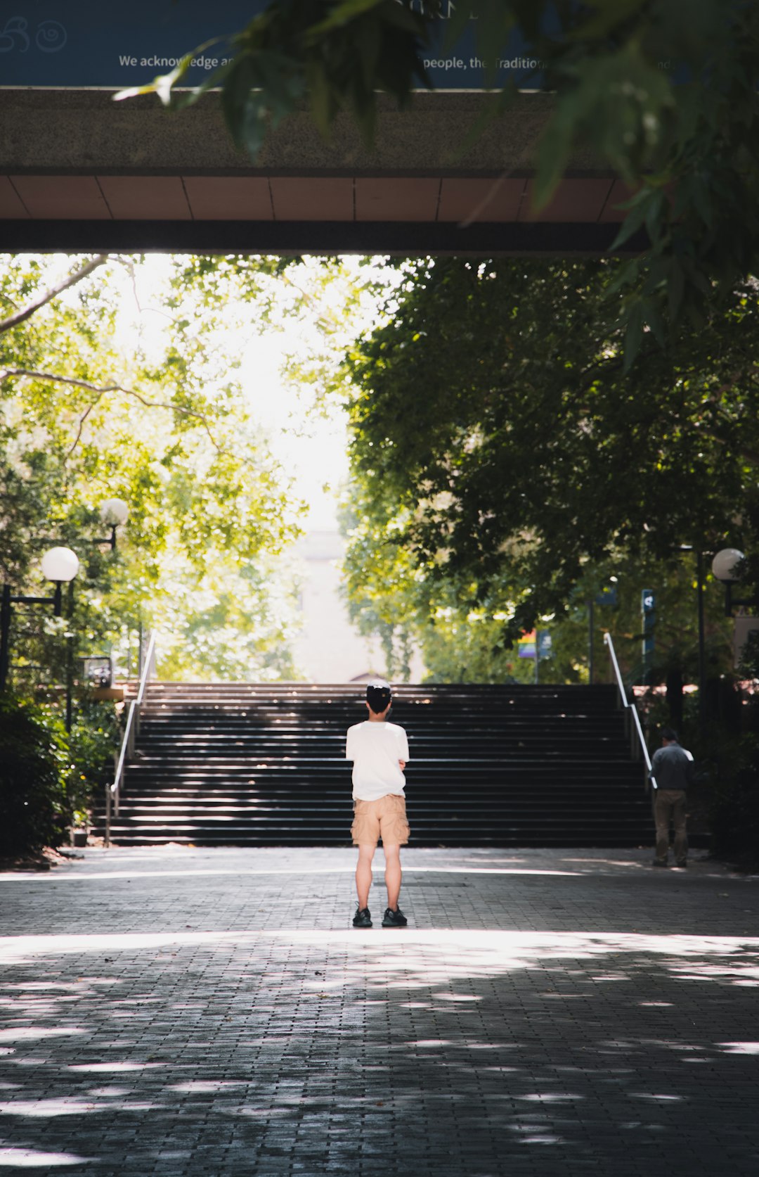 man in white t-shirt and brown shorts walking on sidewalk during daytime