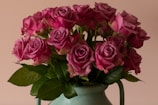 A bouquet of vibrant pink roses is arranged in a green vase. The flowers are fresh and in full bloom, with rich green leaves complementing the pink petals.