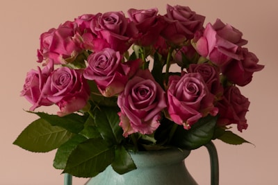 A bouquet of vibrant pink roses is arranged in a green vase. The flowers are fresh and in full bloom, with rich green leaves complementing the pink petals.
