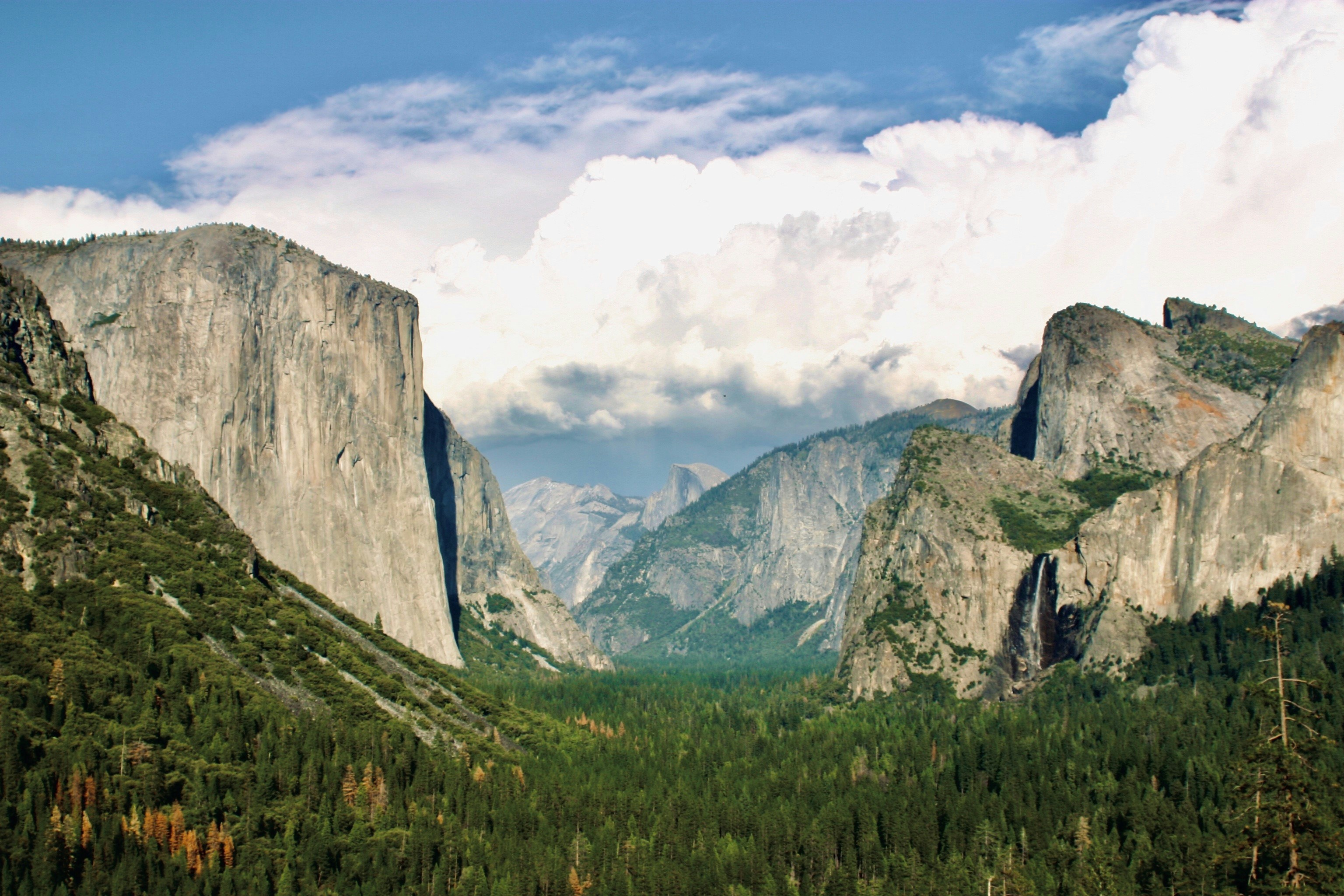 green grass field near mountain under white clouds during daytime