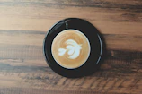 A steaming cup of chai latte with intricate latte art on a rustic wooden table.