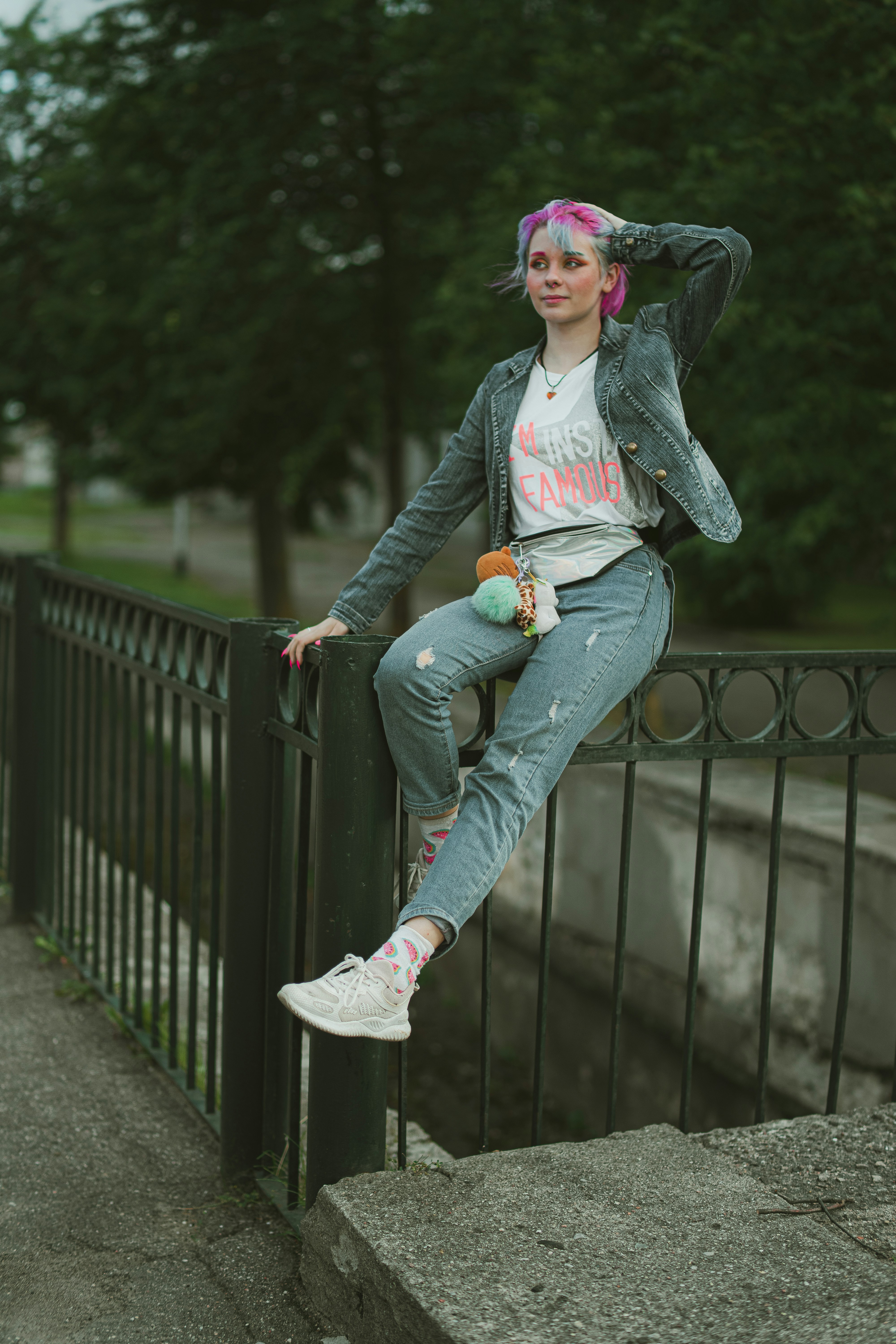 Wanita dengan hoodie abu-abu dan jeans denim biru duduk di pagar logam hitam di siang hari