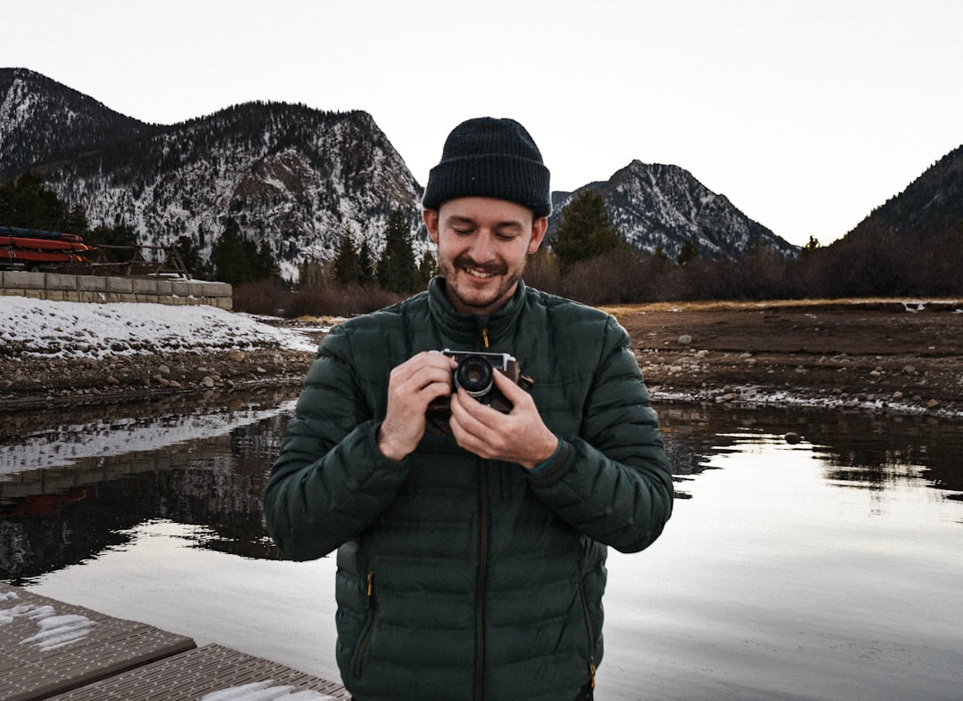 man in green jacket holding black dslr camera