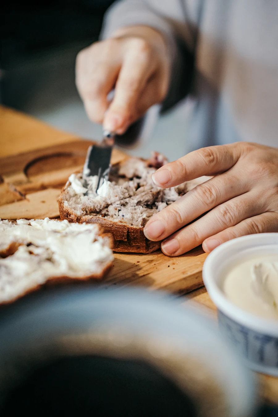 Hands spreading butter on a thick-cut slice of bread on a worn board