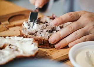 person slicing a bread on a brown wooden chopping board