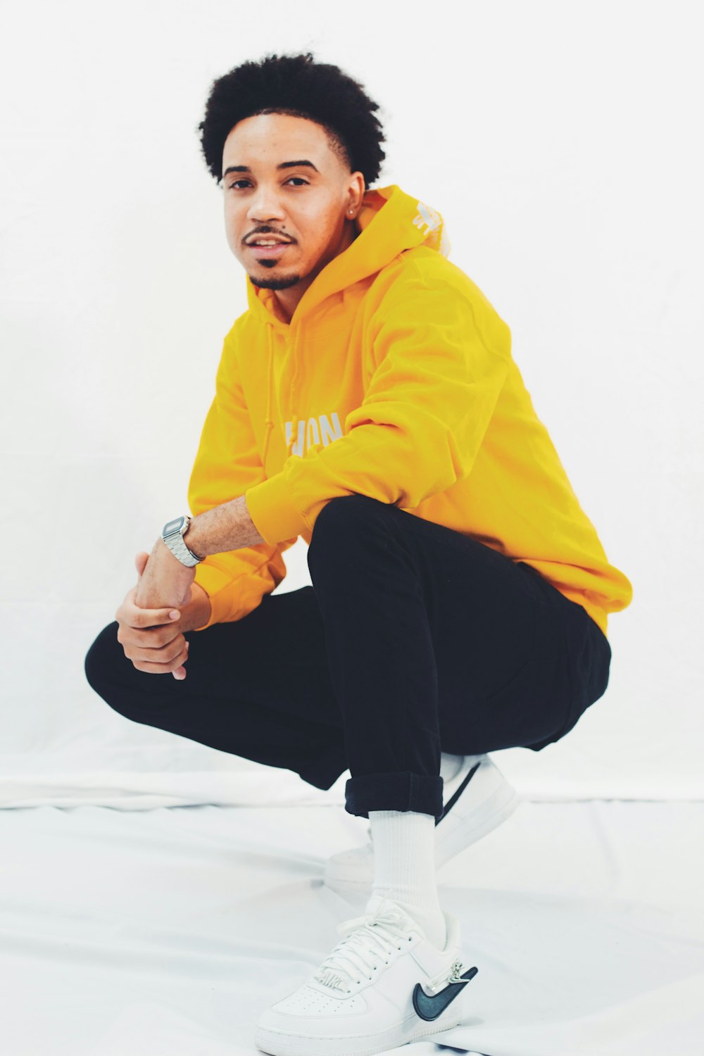 woman in yellow hoodie and black pants sitting on white floor