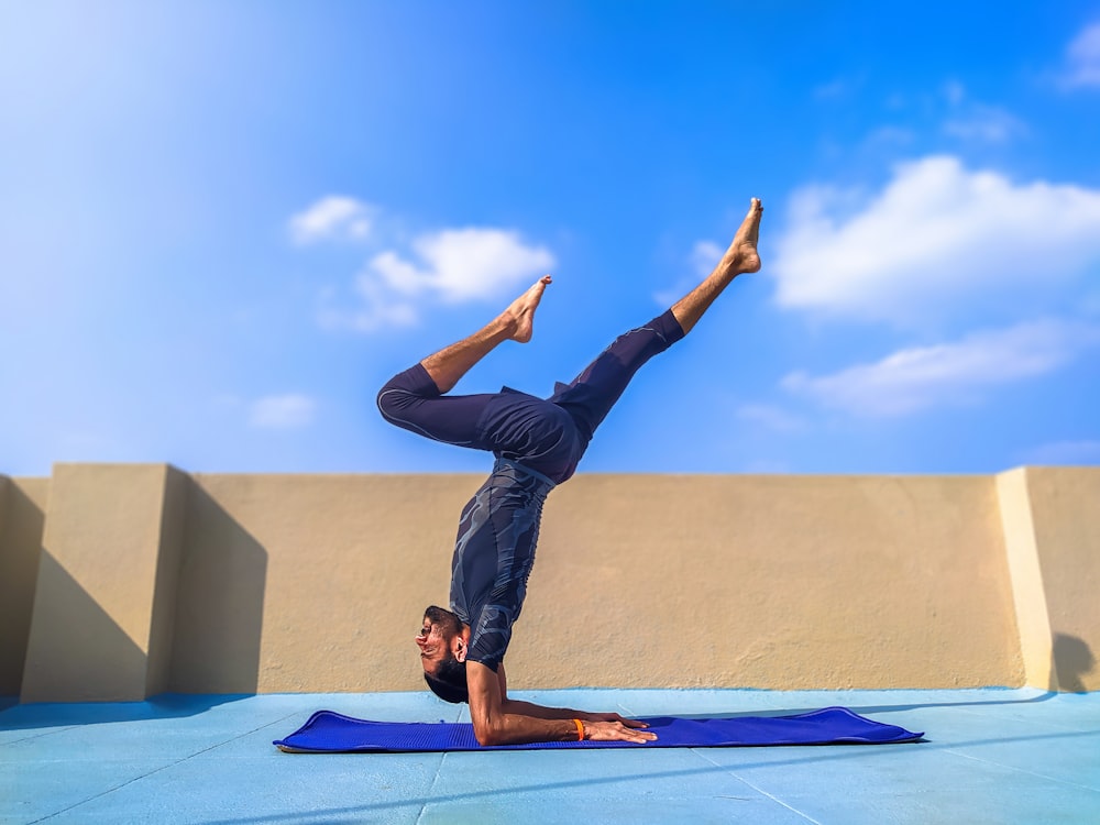 Mann in schwarzer Hose und schwarzem Hemd auf blauer Yogamatte stehend