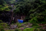 Hiker setting up float tent swiftly on uneven terrain beside a bubbling stream.