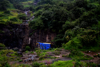A sleek green shower tent pitched beside a flowing mountain stream under a bright blue sky.