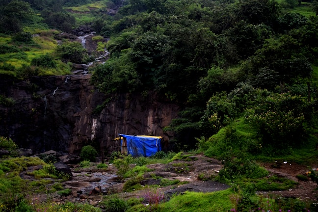 Hiker setting up float tent swiftly on uneven terrain beside a bubbling stream.