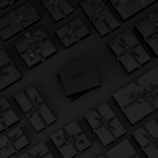 A collection of neatly arranged black gift boxes with ribbons, set on a dark background. One box in the center is slightly raised and has the word 'Bettr' printed on it.
