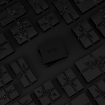 A collection of neatly arranged black gift boxes with ribbons, set on a dark background. One box in the center is slightly raised and has the word 'Bettr' printed on it.