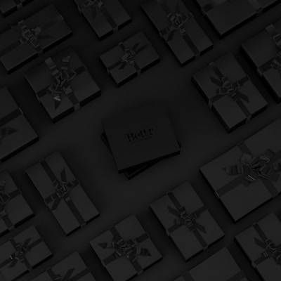 A collection of neatly arranged black gift boxes with ribbons, set on a dark background. One box in the center is slightly raised and has the word 'Bettr' printed on it.