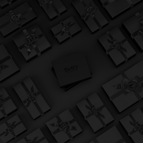 A collection of neatly arranged black gift boxes with ribbons, set on a dark background. One box in the center is slightly raised and has the word 'Bettr' printed on it.