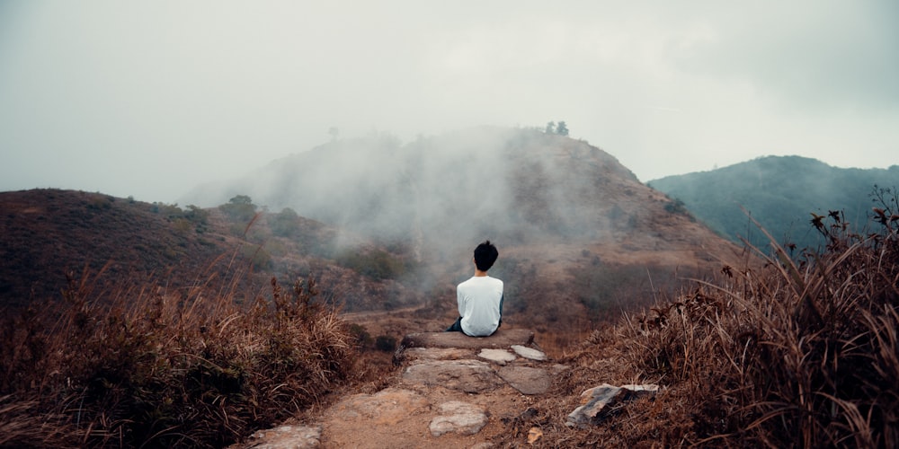 man in white shirt sitting on brown dirt road