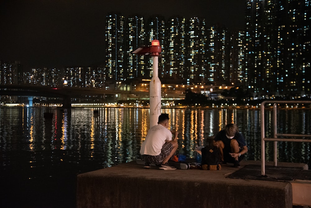 man in white shirt sitting on brown wooden dock during night time