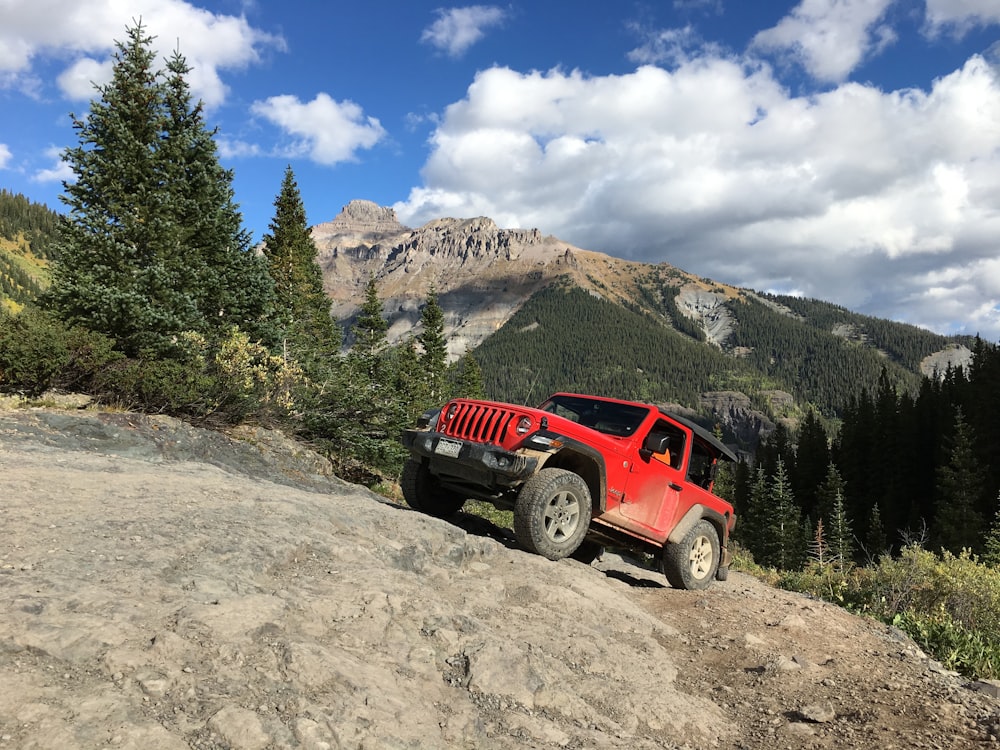 red suv on dirt road near green trees and mountain under blue sky during daytime