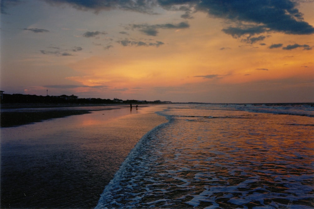 persone che camminano sulla spiaggia durante il tramonto