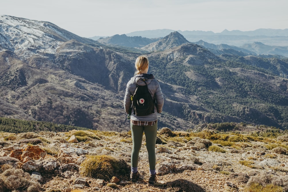 woman in black jacket and gray pants standing on rocky ground during daytime