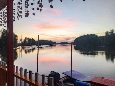 A peaceful lakeside dock at sunset with a small boat gently floating on the water near lush green trees.