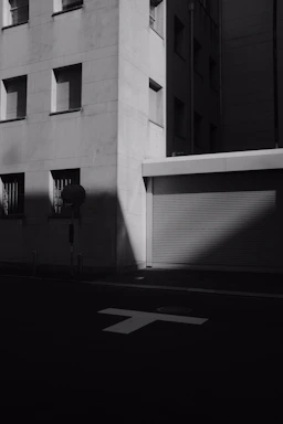 A black and white photo of a bustling city street captured with a Ricoh GR camera, highlighting sharp contrasts and deep shadows.