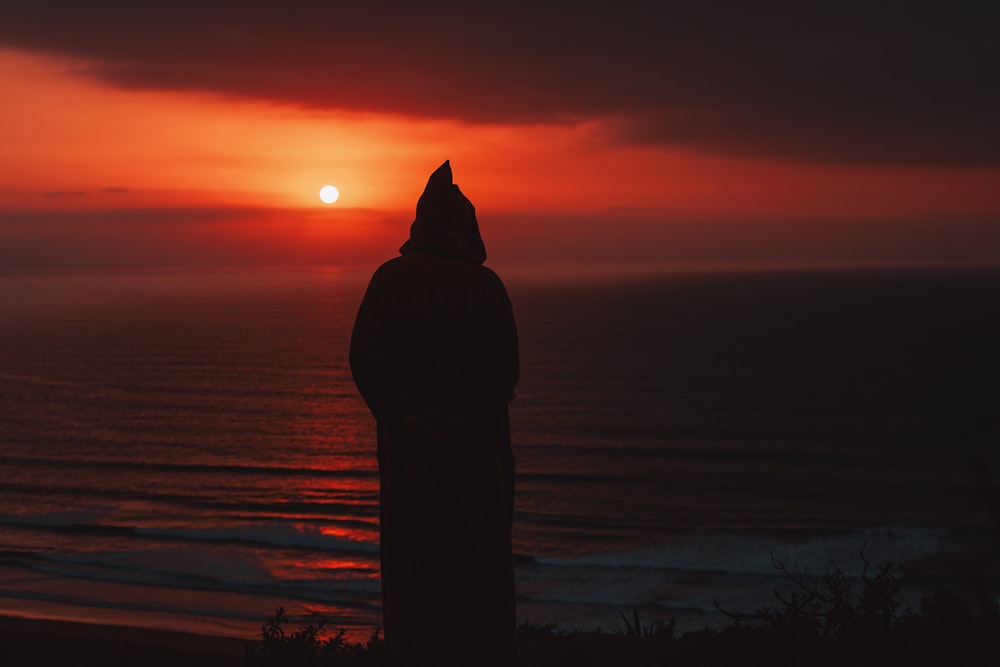 silhueta da pessoa em pé na praia durante o pôr do sol