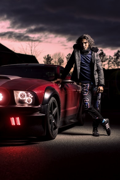woman in black jacket and black pants standing beside red car