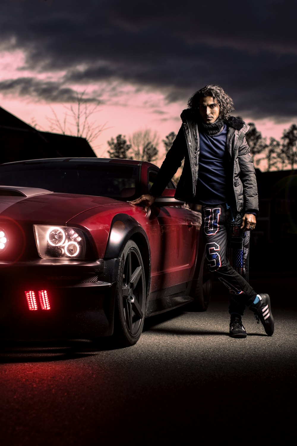 woman in black jacket and black pants standing beside red car