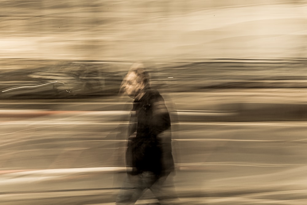 fotografia de lapso de tempo do homem em jaqueta preta andando na estrada durante o dia
