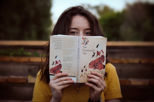 A woman holding a copy of The Handmaid’s Tale by Margaret Atwood sitting on a bench