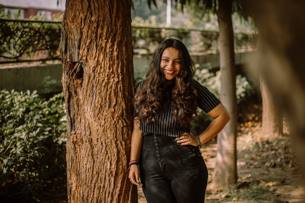 woman in black shirt and blue denim jeans standing beside brown tree