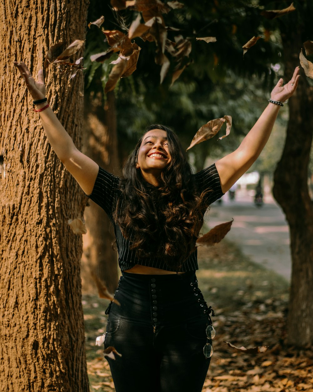woman in black long sleeve shirt and black denim jeans standing beside brown tree trunk during
