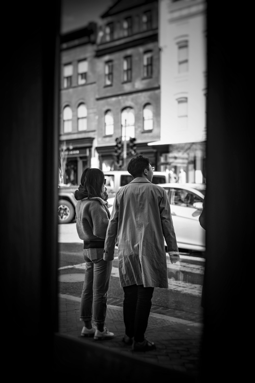 grayscale photo of woman in coat and pants standing in front of car