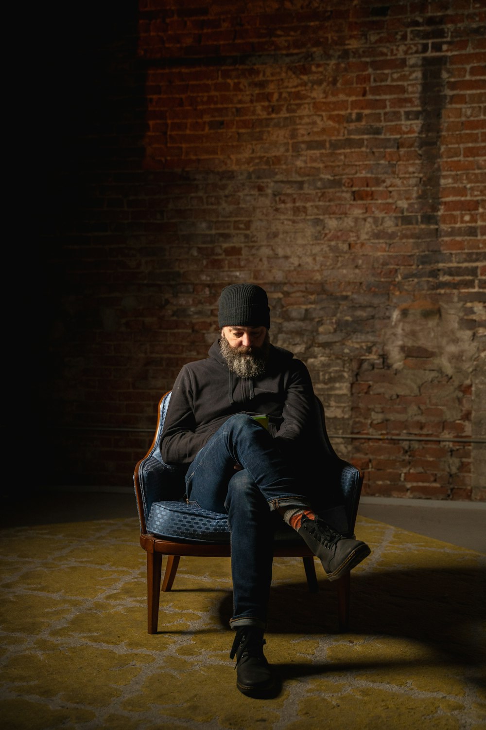 man in black jacket and blue denim jeans sitting on brown wooden chair