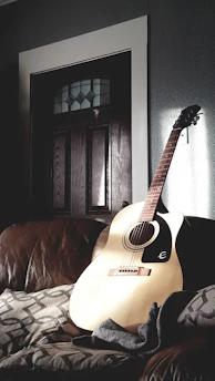 A close-up of a wooden acoustic guitar resting against a soft cushion.