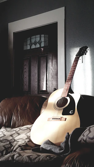 A close-up of a wooden acoustic guitar resting against a soft cushion.