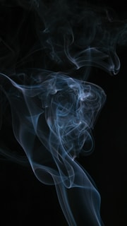 Delicate wisps of smoke curling gently above a dark, reflective surface, evoking mystery and calm.